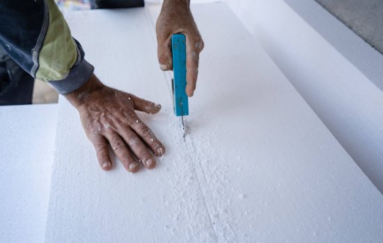 Construction worker using the hand saw to cut the styrofoam insulation panel table at the construction site in the insulating renovation procedure